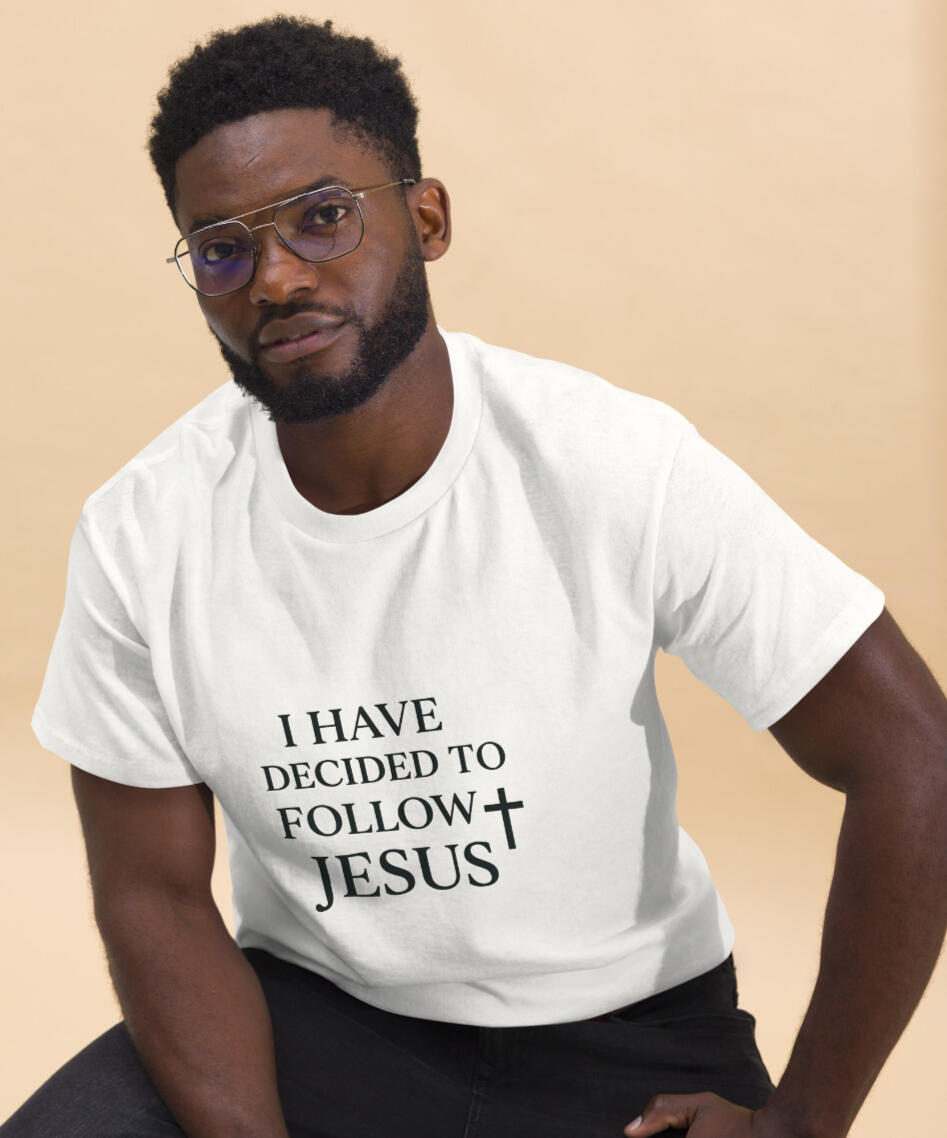 Black man with glasses, seated, modeling Tela Design's Store "I Have Decided to Follow Jesus" Christian 100% cotton white tee, designed for everyday faith and comfort.